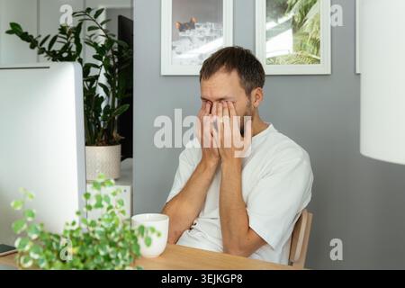 Müde oder verschlafter Mann sitzt am Computer überarbeitet massierenden Augen arbeiten von zu Hause aus auf covid-19 Lockdown Stockfoto