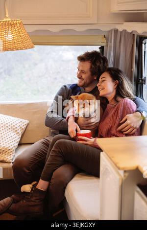 Junge verheiratete Paar in Anhänger oder Wohnmobil sitzen auf dem Sofa kuscheln niedlichen Hund genießen Wochenende zusammen Stockfoto