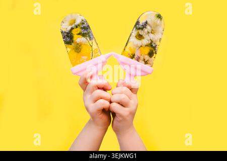 Hand hält hausgemachte Blumen Eis Eis Eis Eis Eis auf gelbem Hintergrund. Sommerkonzept Stockfoto