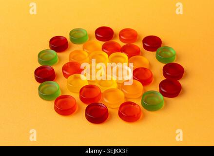 Runde gummiartige Bonbons. Kauen bunter Marmeladetabletten, Gelee Gummitropfen, Gelatinesbonbons auf orangefarbenem Hintergrund von oben Stockfoto