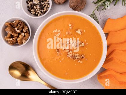 Kürbissuppe mit Walnüssen in einer weißen Schüssel, dekoriert mit Kürbisscheiben und Gewürzen von oben auf weißem Marmorhintergrund Stockfoto