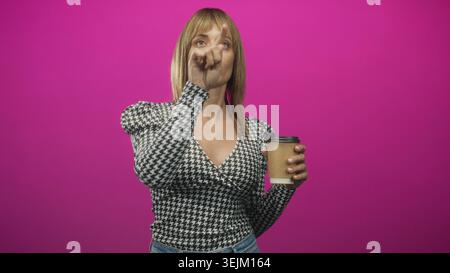 Frau zeigt mit dem Zeigefinger, während sie die braune Kaffeetasse zum Mitnehmen hält und im Studio nach vorne blickt; Entschlossenheit. Stockfoto