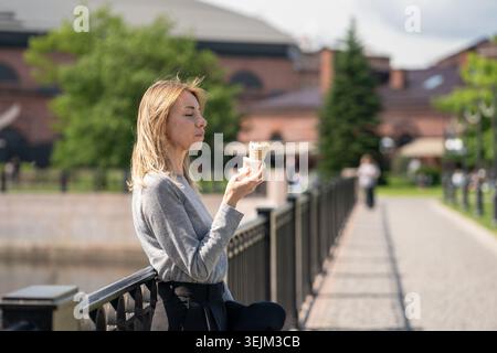 Reizende Geschäftsfrau, die am Sommertag Eiscreme-Snacks genießt, während sie draußen spaziert. Stockfoto