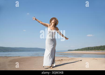 Lifestyle im Sommer. Porträt einer älteren Frau mit Strohhut tanzt im Sommer am Strand Stockfoto