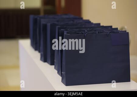 Reihe dunkelblauer Geschenktüten aus Papier am weißen Tresen bei Firmenveranstaltungen Stockfoto