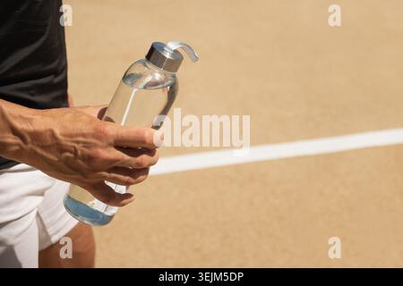 Glasflasche mit erfrischendem Wasser in der Hand des Athleten. Wasserhaushalt für Workout Stockfoto