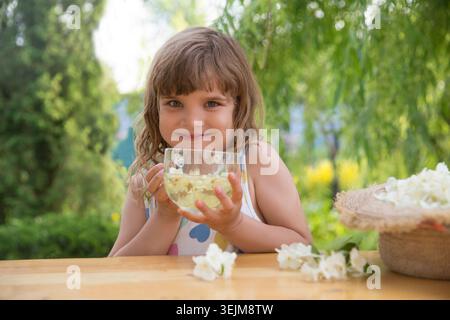 Das Kind sammelt im Sommer Jasminblüten und trinkt Jasmintee an einem Tisch im Garten. Aromatherapie und Spa-Konzept. Stockfoto