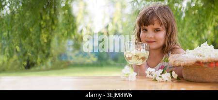 Das Kind sammelt im Sommer Jasminblüten und trinkt Jasmintee an einem Tisch im Garten. Aromatherapie und Spa-Konzept. Stockfoto