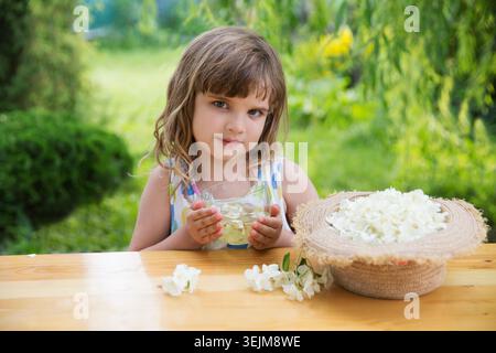 Das Kind sammelt im Sommer Jasminblüten und trinkt Jasmintee an einem Tisch im Garten. Aromatherapie und Spa-Konzept. Stockfoto
