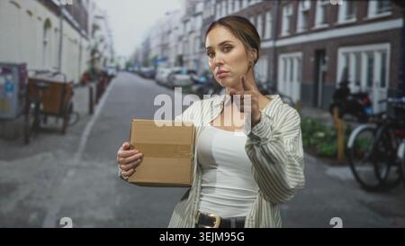 Frau mit Pappkarton zeigt mit direktem Blick und Klebeband den Finger auf der Straße nach vorne; fest durchsetzungsfähig. Stockfoto