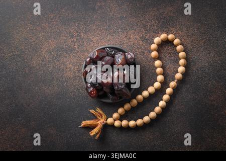 Ramadan. Hölzerne Gebetsperlen und Datteln in einer Schüssel auf Braun. Eid Mubarak. Stockfoto
