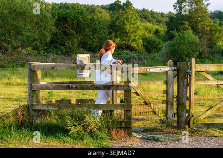 Frau geht durch ein traditionelles hölzernes Kissing Gate auf einem öffentlichen Fußweg in eine sonnige Wiese im Formby Naturreservat, Formby, Großbritannien. Stockfoto