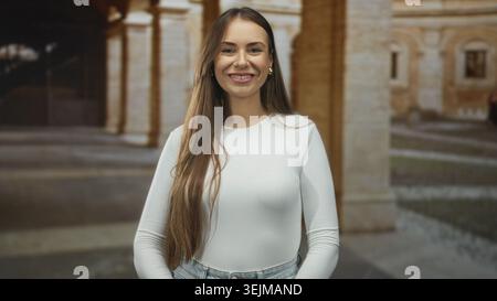 Junge Frau mit langen braunen Haaren, geschlossenen Augen und einem leichten Lächeln, die vor einem Steinkolonnadengebäude steht; Gelassenheit. Stockfoto