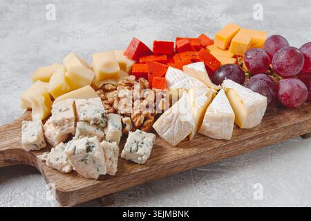 Verschiedene Käsesorten auf einem Holzbrett, mit Trauben und Walnüssen, Vorspeise, keine Leute. Stockfoto