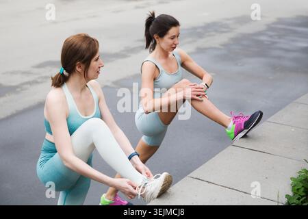 Sportliche zwei Frauen im Sportoutfit, die morgens trainieren und sich auf dem Straßensportplatz Strecken. Fitness Workout auf dem Sport Gr Stockfoto