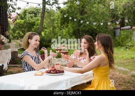 Drei junge schöne lächelnde Frau haben Spaß zusammen und trinken Wein im Sommergarten weibliche Freunde, die einen Urlaub im Freien genießen Stockfoto
