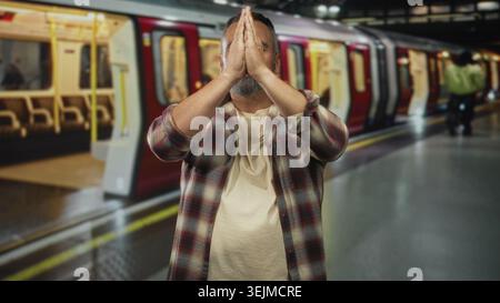 Mann mit zusammengedrückten Händen über dem Kopf, Augen geschlossen, auf einem Bahnsteig im Bahnhofsgebäude stehend; ruhige Reflexionsabsicht. Stockfoto