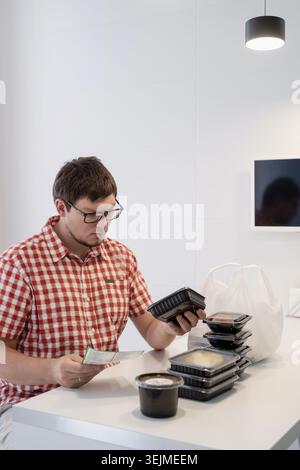 Ein junger Mann, der in der modernen Küche Essenskisten sortiert Stockfoto