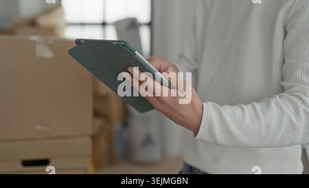 Mann, der Tablets hält und gestapelte Umzugskartons und Pakete im Gebäude überprüft; fokussierte Bestandsverwaltung. Stockfoto