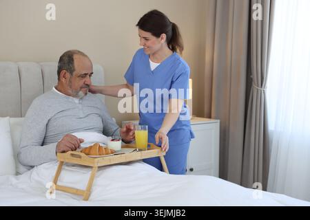 Die Pflegekraft frühstückt einem älteren Mann zu Hause im Bett Stockfoto