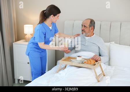 Die Pflegekraft frühstückt einem älteren Mann zu Hause im Bett Stockfoto