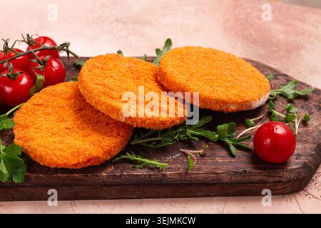 Knusprig gebratene Fischkoteletts, Fischburger, auf Holzschneidebrett, mit Rucola und Kirschtomaten, hausgemacht, keine Leute, Stockfoto