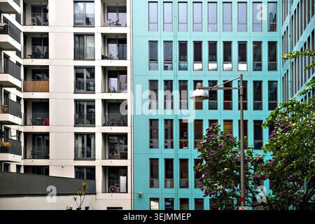 Berlin, Deutschland , 3. Mai 2026, Kontrast zwischen einer weißen Balkonfassade der Wohnung und einer hell türkisfarbenen Bürogebäudewand mit Straßenlaterne. Stockfoto