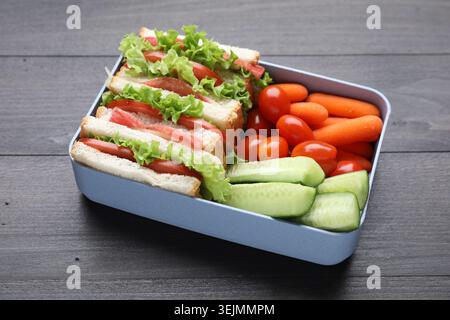 Lunchbox mit leckeren Sandwiches und Gemüse auf dunklem Holztisch, Nahaufnahme Stockfoto