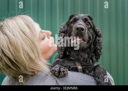 Eine junge Frau, die ihren Cocker Spaniel Hund auf grünem Hintergrund hält Stockfoto