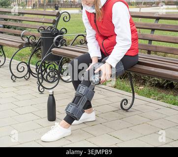 Frau, die Knie- oder Orthesen nach Beinoperationen trägt, im Park spazieren geht Stockfoto