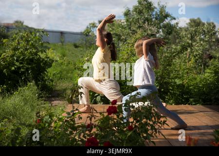 Familie Mutter und Kind Tochter üben Yoga im Freien. Familie trainiert gemeinsam im sonnigen Hinterhof. Stockfoto