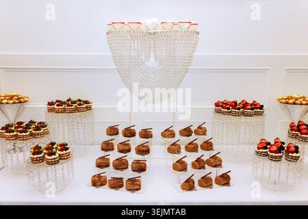 Desserts werden auf Tischen für Festveranstaltungen, Kuchen, Gebäck und frisches Obst in einem hellen Raum platziert Stockfoto