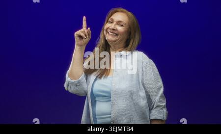 Die ranghöchste hispanische Frau zeigt den Zeigefinger im Studio mit der rechten Hand vor tiefblauem Hintergrund und macht eine warnende Geste; selbstbewusste Erinnerung. Stockfoto