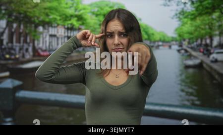 Die Frau zeigt den Finger nach vorne und den Finger auf den Tempel auf der Straße mit einem Herzring sichtbar; Anschuldigungsspannung. Stockfoto