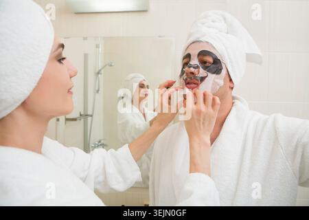 Junger Mann im weißen Morgenmantel, der sich mit Gesichtsmaske entspannt Stockfoto