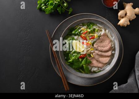 Pho Bo Suppe mit Rindfleisch in Schüssel auf schwarzem Hintergrund. Vietnamesische Küche. Stockfoto