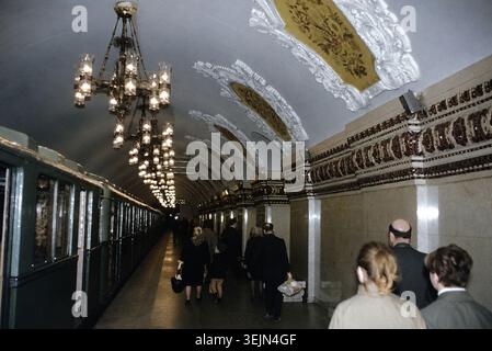 Sowjetunion der 1960er Jahre in Farbe - U-Bahn-Station Kiewskaja, Moskau, UdSSR, fotografiert in den 1960er Jahren Pendler laufen entlang des Bahnsteigs neben einem grünen Zug unter kunstvollen Kronleuchtern und reich verzierten Gipsdecken mit Blumenmotiven und vergoldeten Paneelen. Das opulente Design des Bahnhofs veranschaulicht die stalinistische Architektur und die Pracht der Moskauer U-Bahn während der Sowjetzeit. Stockfoto