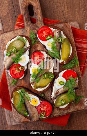 Offene Sandwiches mit Sprotten, Gemüse und Kräutern, auf Holzbrett, Frühstück, Snack, Stockfoto