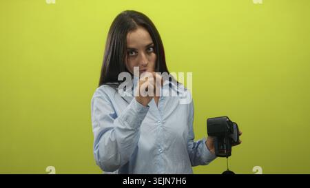 Frau in hellblauem Hemd, die Kamera mit dem Finger in der rechten Hand in einem hellgrünen Studio hält; ernste Warnung. Stockfoto