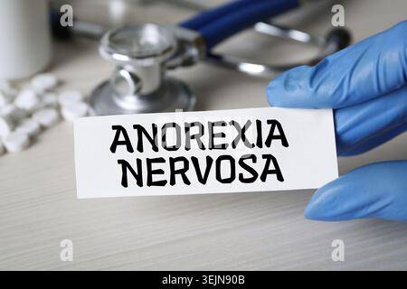 Doktor hält Karte mit den Worten Anorexia nervosa am Tisch, Nahaufnahme Stockfoto