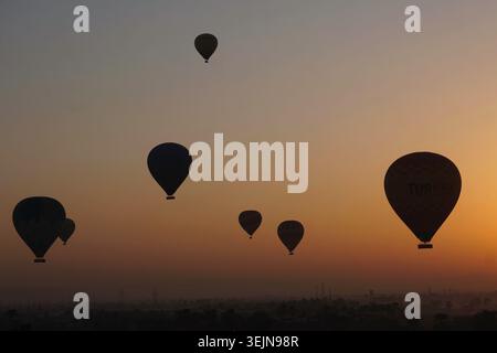 Mehrere Heißluftballons, die während des Sonnenaufgangs in der Nähe von Luxor, Ägypten, aufsteigen und eine atemberaubende Luftkulisse über der historischen Wüstenlandschaft schaffen. Stockfoto