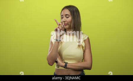 Frau zeigt mit dem Finger nach oben, die Arme sind an der Taille gefaltet, im Studio mit kalkgrünen Wänden; durchdachte Entscheidung. Stockfoto