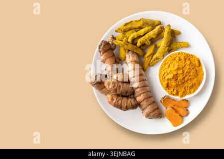 Kurkuma als frische, trockene Wurzel, Kurkumapulver und geschnittene Pflanze in Teller auf Beige. Flache Lagen. Blick von oben. Leerzeichen für Text. Stockfoto