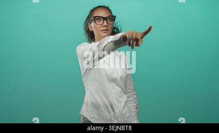 Frau zeigt mit dem Finger nach rechts mit Brille und weißem Hemd im Studio; Vertrauen in die Anweisung. Stockfoto