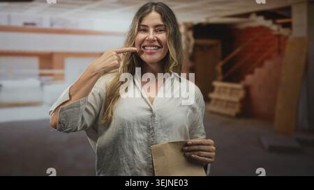 Frau zeigt mit dem Finger auf den Tempel, der Papiertüte im Gebäude mit sichtbaren Treppen und Holzpalette hält; Selbstbewusstsein Klugheit. Stockfoto
