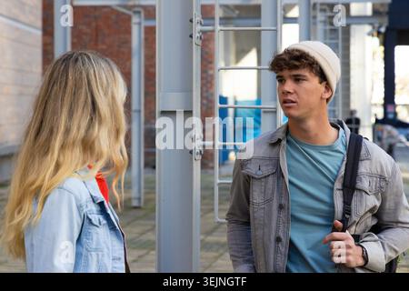 Teenager-Studenten plaudern in der Nähe von Metalltor und Pfosten im Campus-Hof, einer trägt einen Rucksackgurt. Duo, Freunde, Urban, Outdoo Stockfoto