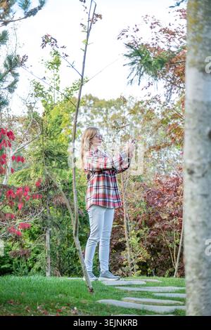 Frau, die die Natur genießt, steht im Japanischen Garten und macht Fotos auf dem Smartphone Stockfoto