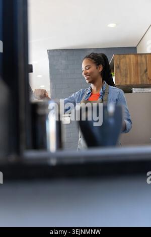 Afroamerikanische Barista, die Espresso in grauer Schürze zubereiten und Milchkännchen halten. Kaffee, Brühen, Maschine, den Stockfoto