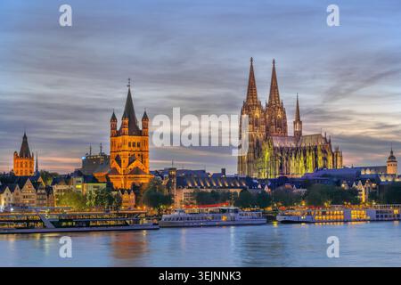 Kölns historisches Zentrum mit Blick auf den Dom und St. Martin am Abend vom Rhein in Deutschland. Beleuchtete Stadtarchitektur Stockfoto