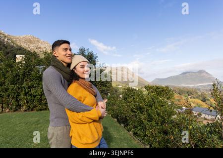 Verschiedene Paare stehen auf einer grasbewachsenen Terrasse am Hügel, tragen Strickpullover und Beanie, Kopierraum. Romantik, Natur, Landschaft, m Stockfoto